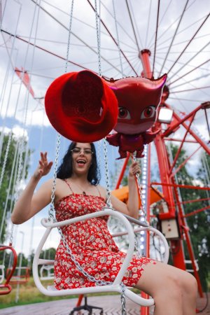 Sally Hunter laughs on a swing ride in a red dress holding a plush toy surrounded by trees and a soccer goal — Sally Hunter #1