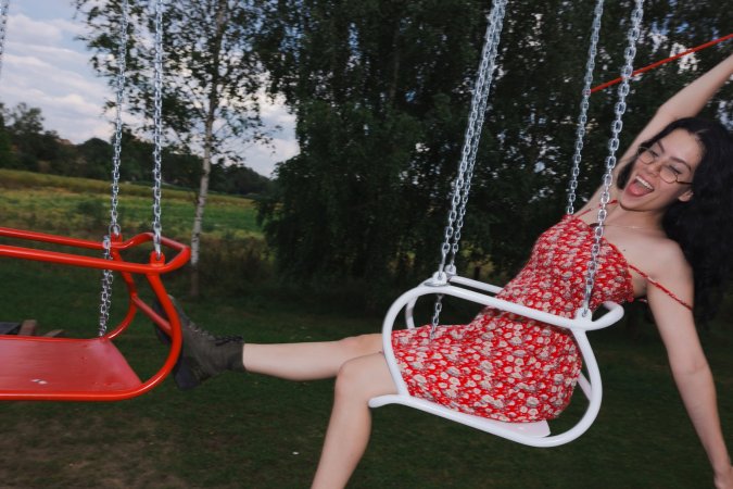 Sally Hunter laughs on a swing ride in a red dress holding a plush toy surrounded by trees and a soccer goal — Sally Hunter #6