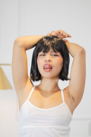 Lilith Baph in white lingerie on a green chair, licking her finger with her tattooed legs spread — Lilith Baph #9