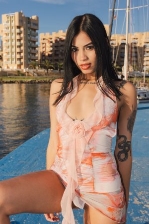 Sofia sits bare-legged on a blue marina dock in a sheer swimsuit, teasing with no underwear as boats drift behind her — Sofia #6
