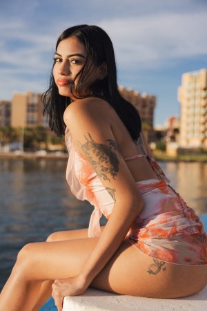 Sofia sits bare-legged on a blue marina dock in a sheer swimsuit, teasing with no underwear as boats drift behind her — Sofia #16
