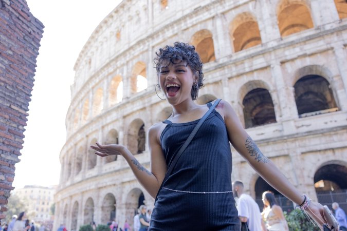 Lilith Baph poses solo in Rome with the Colosseum behind her, black dress and hoop earrings on display — Lilith Baph #2