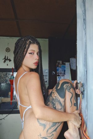 Lilith Baph in white bikini poses with leg up showcasing her tattooed curves and braids indoors — Lilith Baph #2