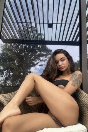 Dulce teases with her tongue out and hand on thigh in black lingerie, posing solo outdoors on a wicker chair #11
