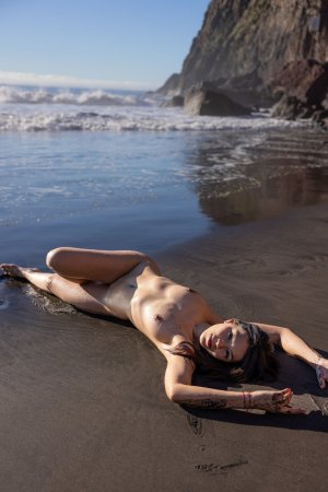 Sky Moon bending over rainbow towel on black sand beach, sunlight warming her naked curves — Sky Moon #10
