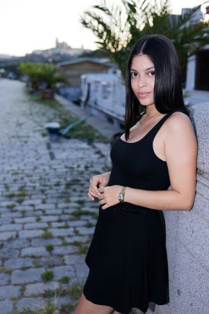 Gia Rosse leans against stone wall in black dress outdoors posing with gold necklace and wristwatch — Gia Rosse #1