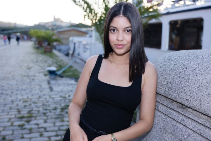 Gia Rosse leans against stone wall in black dress outdoors posing with gold necklace and wristwatch — Gia Rosse #2