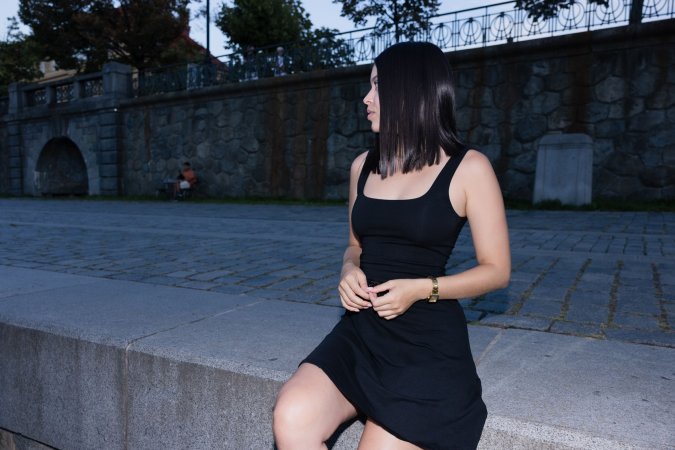 Gia Rosse leans against stone wall in black dress outdoors posing with gold necklace and wristwatch — Gia Rosse #6