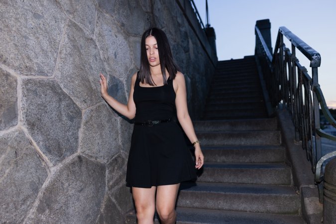 Gia Rosse leans against stone wall in black dress outdoors posing with gold necklace and wristwatch — Gia Rosse #11