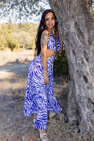 Dulce starts demure in a blue white dress then poses bare midriff against a tree outdoors — Dulce #1