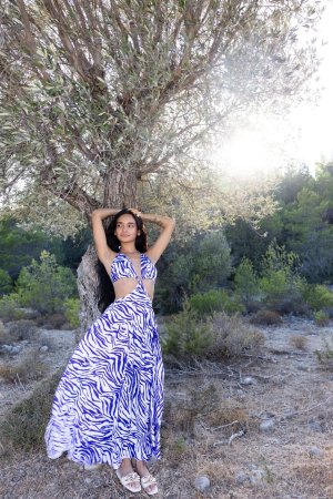 Dulce starts demure in a blue white dress then poses bare midriff against a tree outdoors — Dulce #4