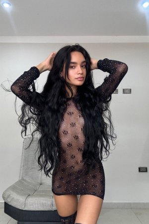 Dulce teases with her yellow toy in sheer black lingerie, legs spread wide on the couch — Dulce #12