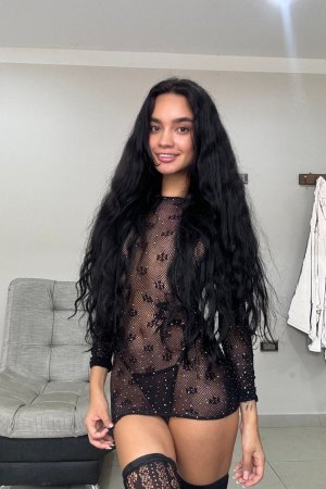 Dulce teases with her yellow toy in sheer black lingerie, legs spread wide on the couch — Dulce #21
