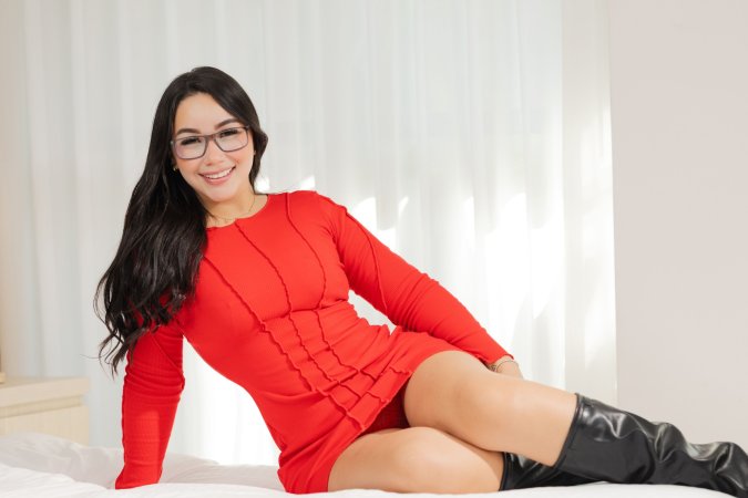 Annie Ferreira in red dress and black boots poses solo by window showing her curvy body and natural assets — Annie Ferreira #2