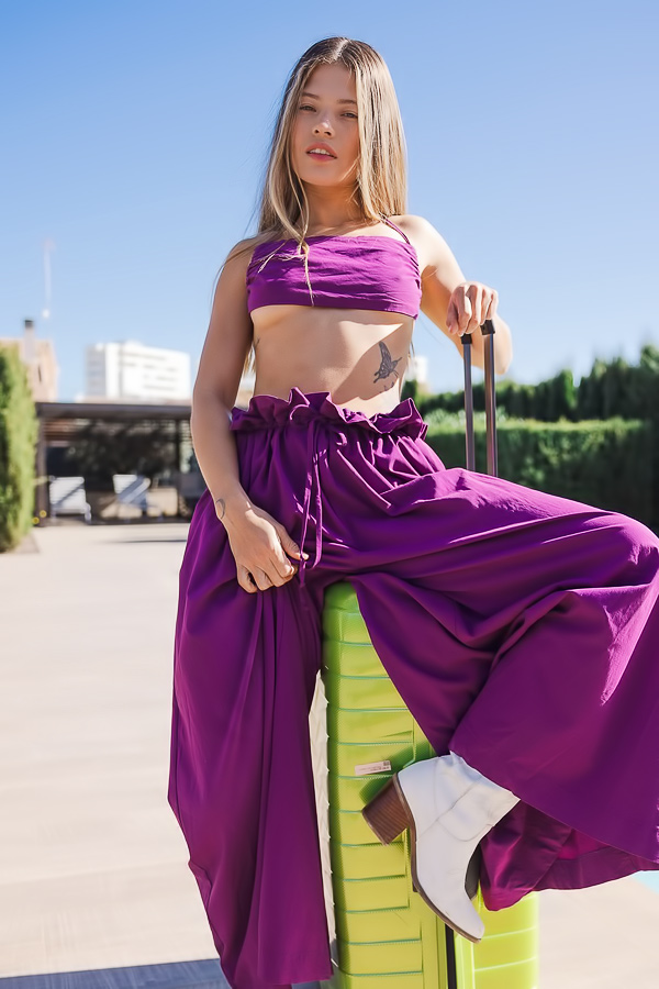 Irene Rouse strips by the poolside in her purple dress, sun flare catching her bare skin as she grips the suitcase handle
