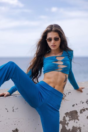 Irene Rouse teases by the ocean in blue, posing solo on a concrete wall with long hair and tattoo — Irene Rouse #3