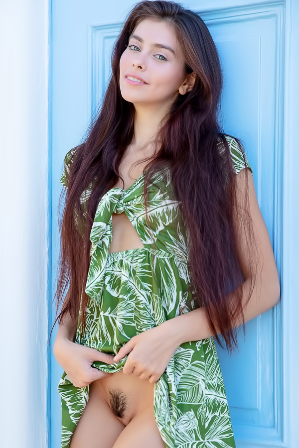 Alissa Foxy leans against a blue door in a green leaf dress, lifting the hem to reveal her bare pussy as she poses solo
