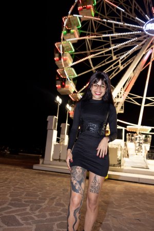 Lilith Baph smiles bold in black dress at night carnival, posing with gun and stick, teasing with every curve — Lilith Baph #4