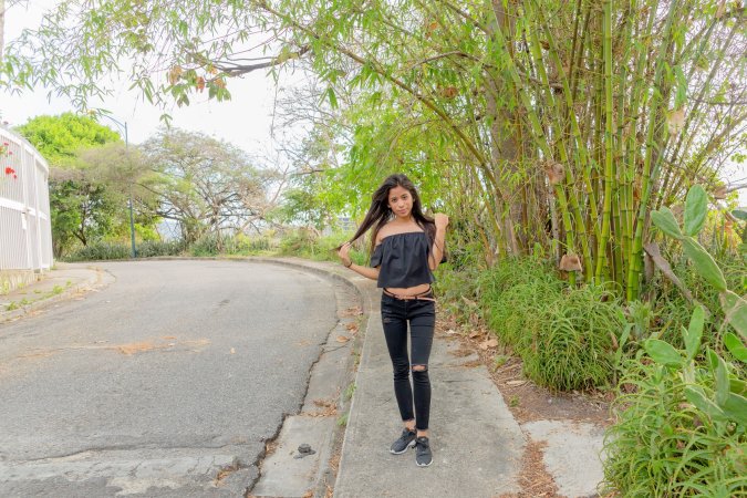 Karin Torres poses solo on a leafy path, black off shoulder top riding up over her hips, long hair swaying with each turn — Karin Torres #1