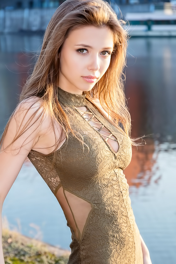 Milla in lace bodysuit posing by water glistening in natural light with cutout details showing skin