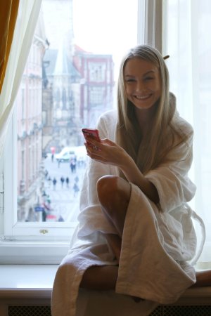 Nancy A in white bathrobe sitting on bed scrolling pink phone bare feet exposed legs — Nancy A #3