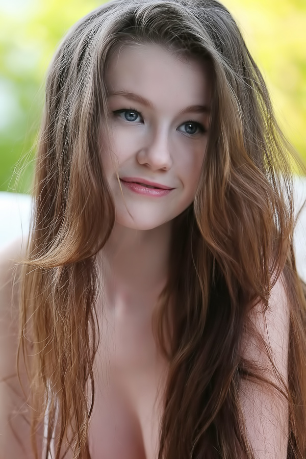 Emily spreading her legs outdoors, smiling while posing nude on white pillows in natural light