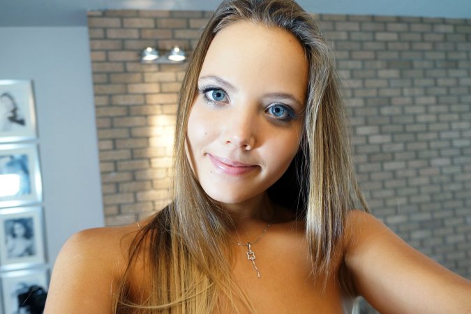 Clover stands bare against brick walls, robe slipping as she poses with camera, nude curves gleaming under soft light — Clover #10