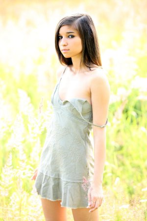 Nika posing in a green dress outdoors in a sunlit field showing her legs and curves — Nika #1