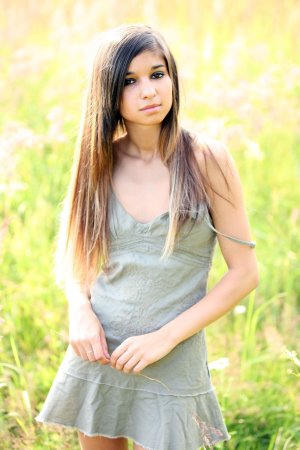Nika posing in a green dress outdoors in a sunlit field showing her legs and curves — Nika #2